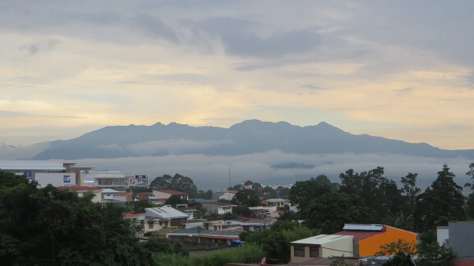 A band of low cloud lying along a long mountain ridge above the rooftops and trees of a San José suburb.