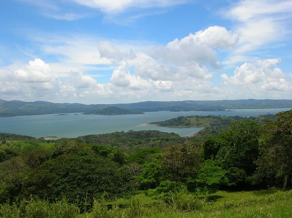 Lake Arenal seen from a hillside, with a wooded peninsula reaching into the water and forested ridges on the far shore.