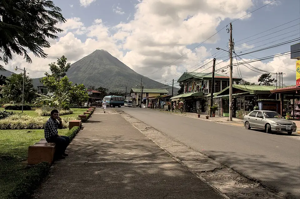 A street in La Fortuna de San Carlos lined with shops and a minibus, with the cone of Arenal volcano rising behind the town.